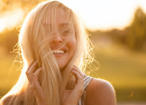 Photo of a blonde woman hiding her face from the sun with her hair